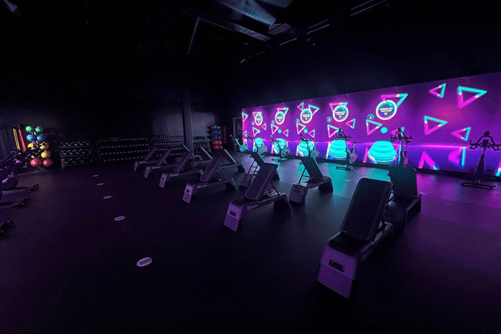A dark Lumin studio with bikes and neon shapes on the wall screens