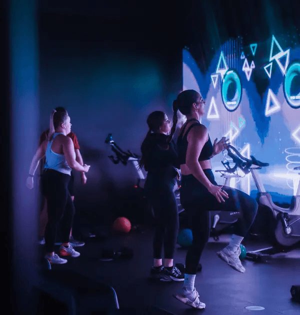 People on bikes in front of a neon-lit wall screen in the Lumin studio